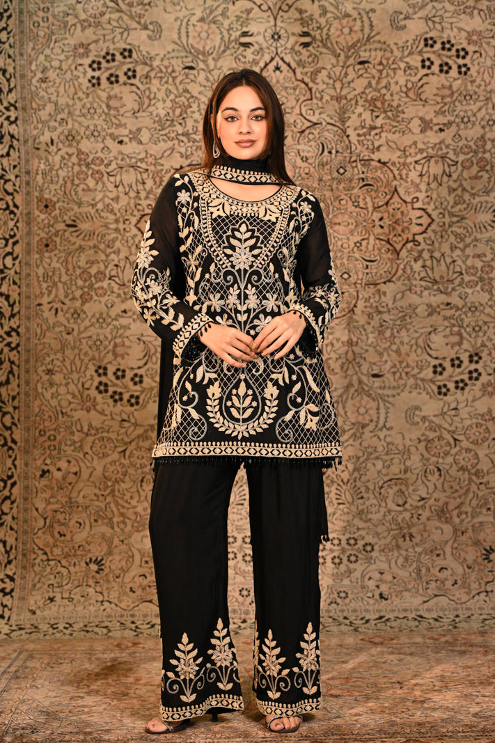 Woman wearing a black and gold embroidered outfit against a patterned wall.